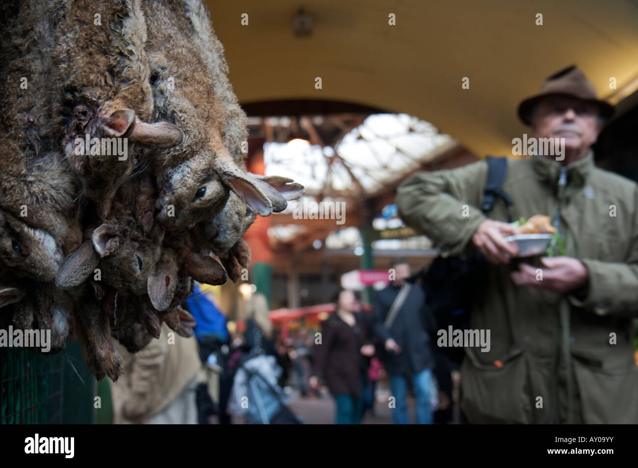 Hasen aufgereiht zum Verkauf in London Borough Market, während ein Mann mit einem Kuchen im Hintergrund vorbeigeht Stockfoto