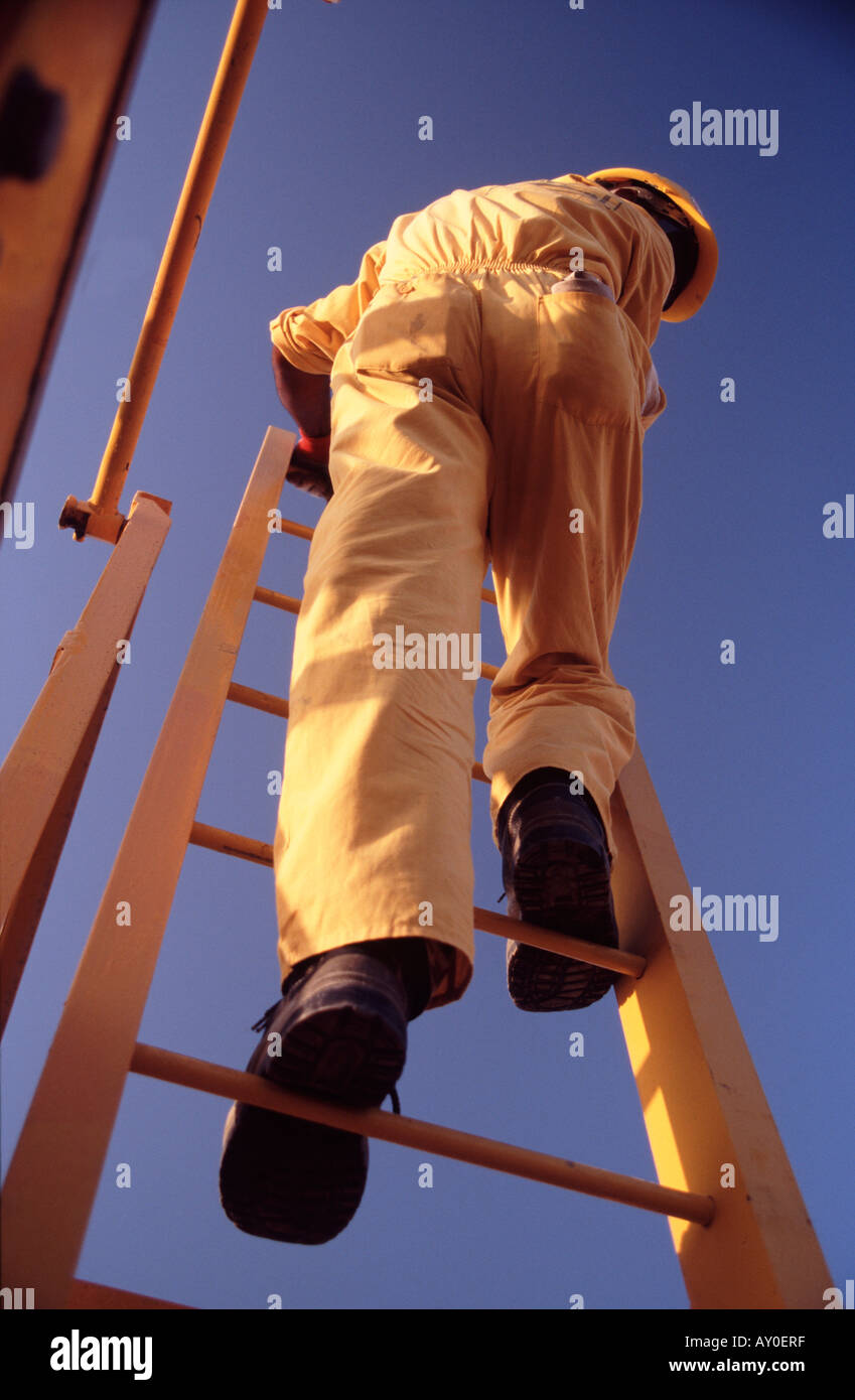 Omanische Arbeiter Klettern auf industriellen Leiter gelb Schutzkleidung an eine petrochemische Anlage in Oman Nahost Stockfoto