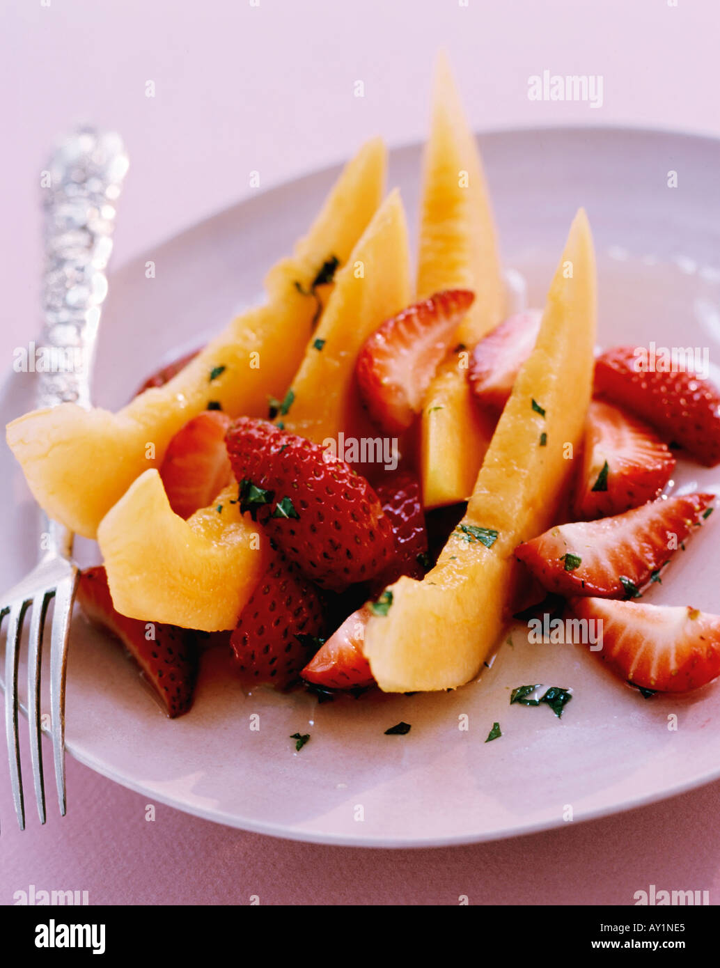 Obstsalat aus Melonenscheiben mit geviertelten Erdbeeren mit Minze-Sirup Stockfoto