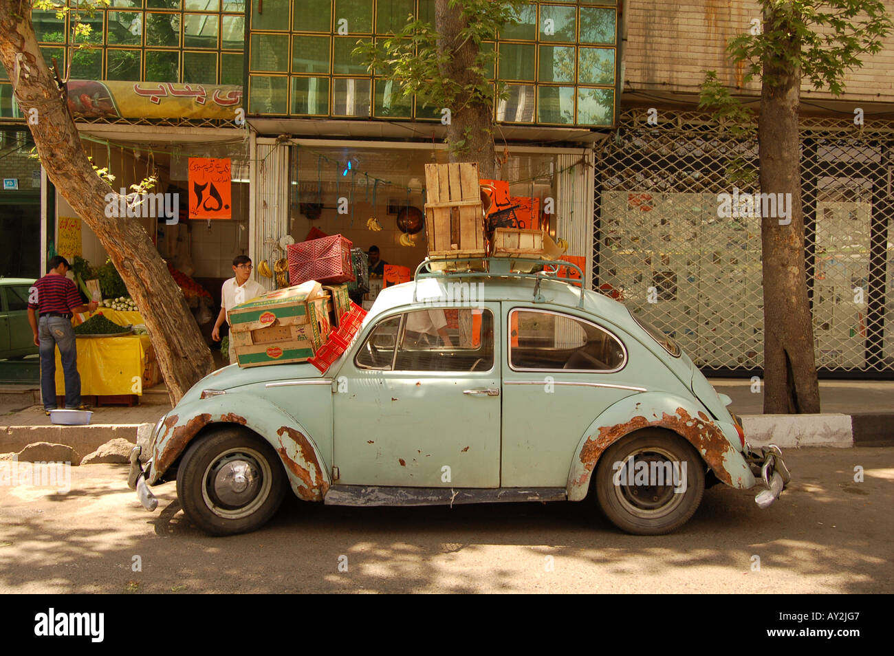Ein rostiger, hellblauer VW-Käfer-Oldtimer, der neben einem Obststand im Freien auf einer Straße in Teheran, Iran, geparkt wurde. Stockfoto