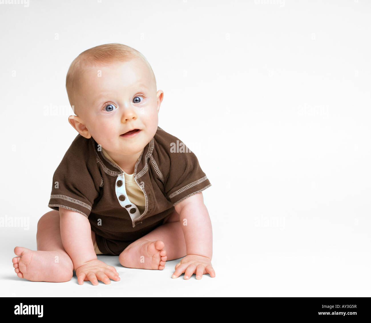 Baby Junge sitzt auf weißem Hintergrund. Lächelnd, braune Kleidung helle Augen interessiert lebhaften Ausdruck Stockfoto