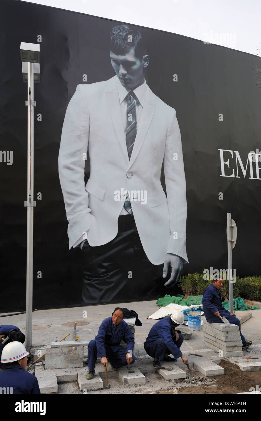 Chinesische Arbeiter ebnen Fliesen vor eine riesige Plakatwand von Emporio Armani in Beijing CBD, China. 3. April 2008 Stockfoto