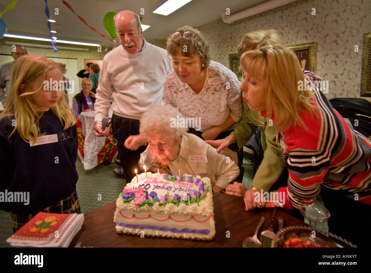 Unterstützt von Familie und Freunden, die einen hundertjährigen, die Kerzen auf ihrem Kuchen während ihrem 100. Geburtstag in einem Pflegeheim bläst Stockfoto