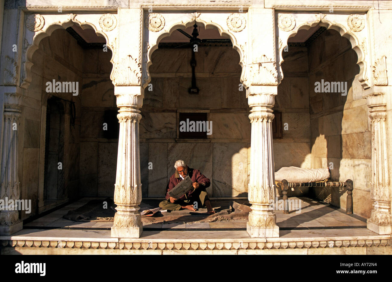 Mann, sitzen, lesen eine Zeitung hinter Marmorbögen im Deshnoke Tempel in der Nähe von Bikaner in Rajasthan Indien Stockfoto