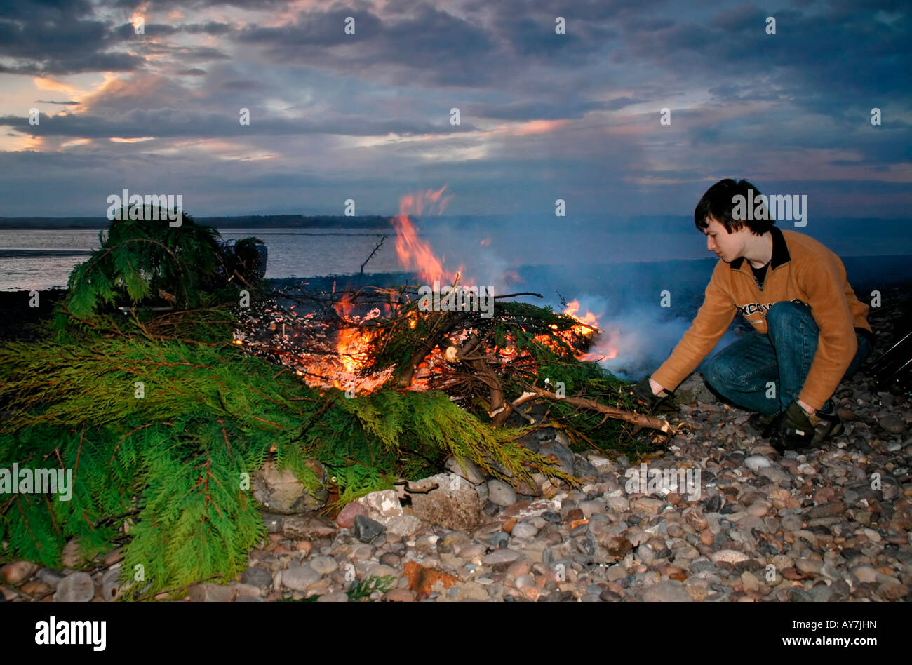Ein Teenager kümmert sich um ein Lagerfeuer gemacht vom Baum Stecklinge von einem Garten. Stockfoto