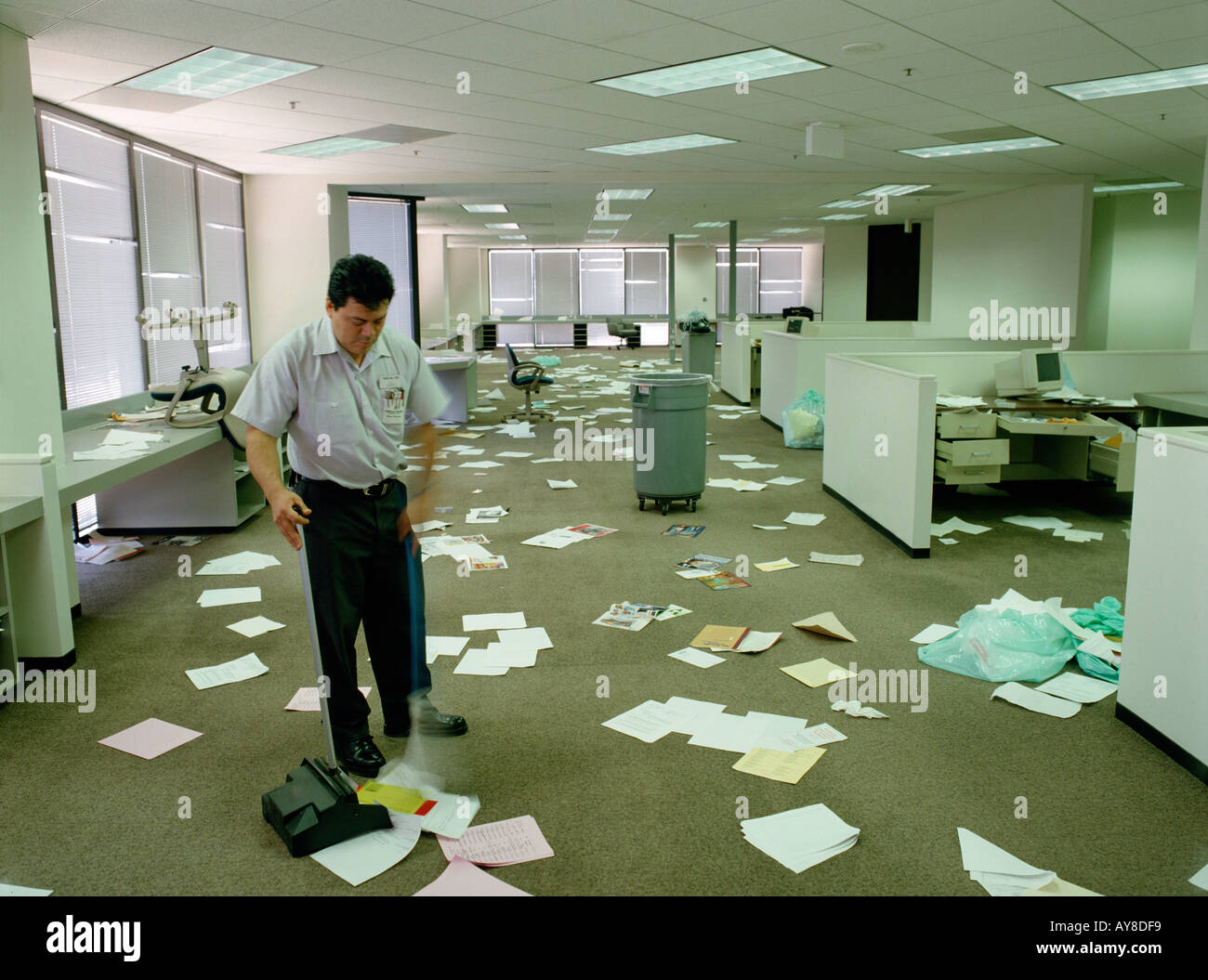 Hauswart fegt Papierkram durcheinander, nachdem Mitarbeiter von Highrise Büro gegangen sind Stockfoto