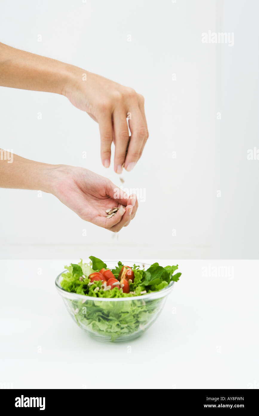 Frau Beregnung Sonnenblumenkerne auf Salat, beschnitten Blick auf Händen Stockfoto