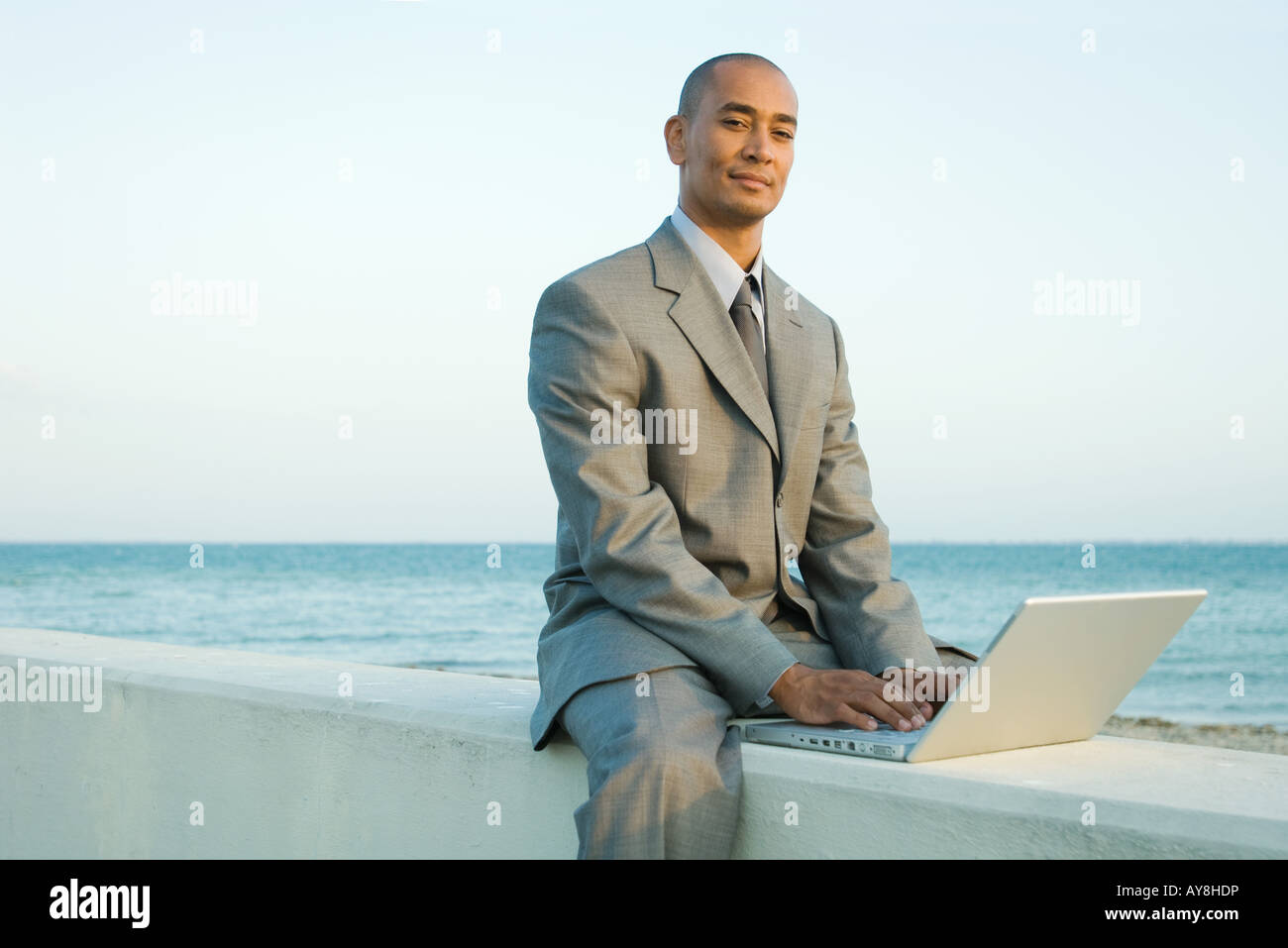 Geschäftsmann, sitzen auf niedrigen Mauer am Meer, mit Laptop-Computer, lächelnd in die Kamera Stockfoto
