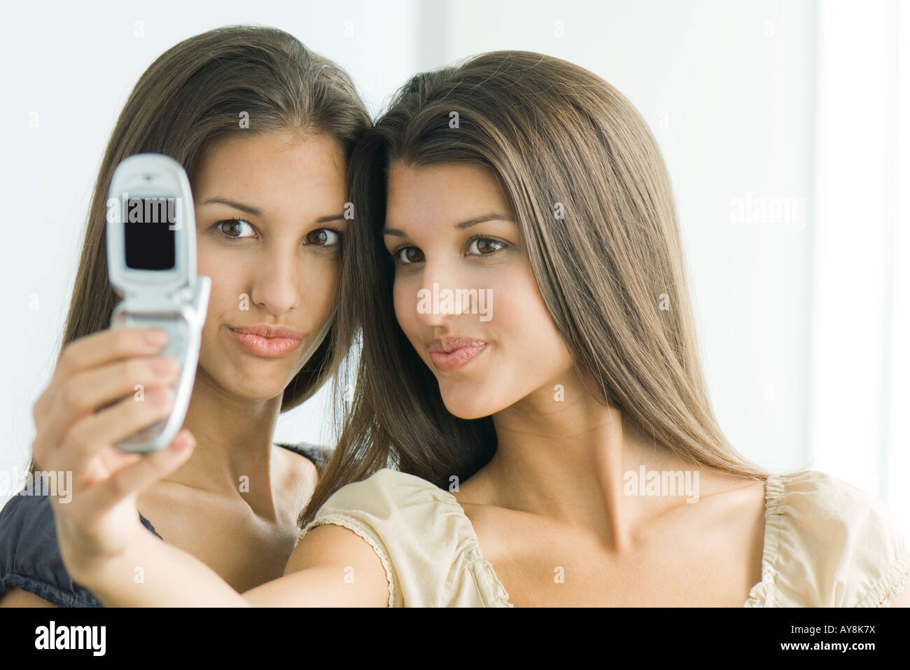 Teenager-Mädchen fotografieren selbst und Zwillingsschwester mit Handy,  beide machen Gesichter Stockfotografie - Alamy