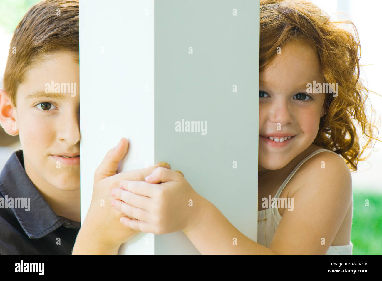 Bruder und Schwester spähen um Spalte in die Kamera, Hand in Hand, Lächeln Stockfoto