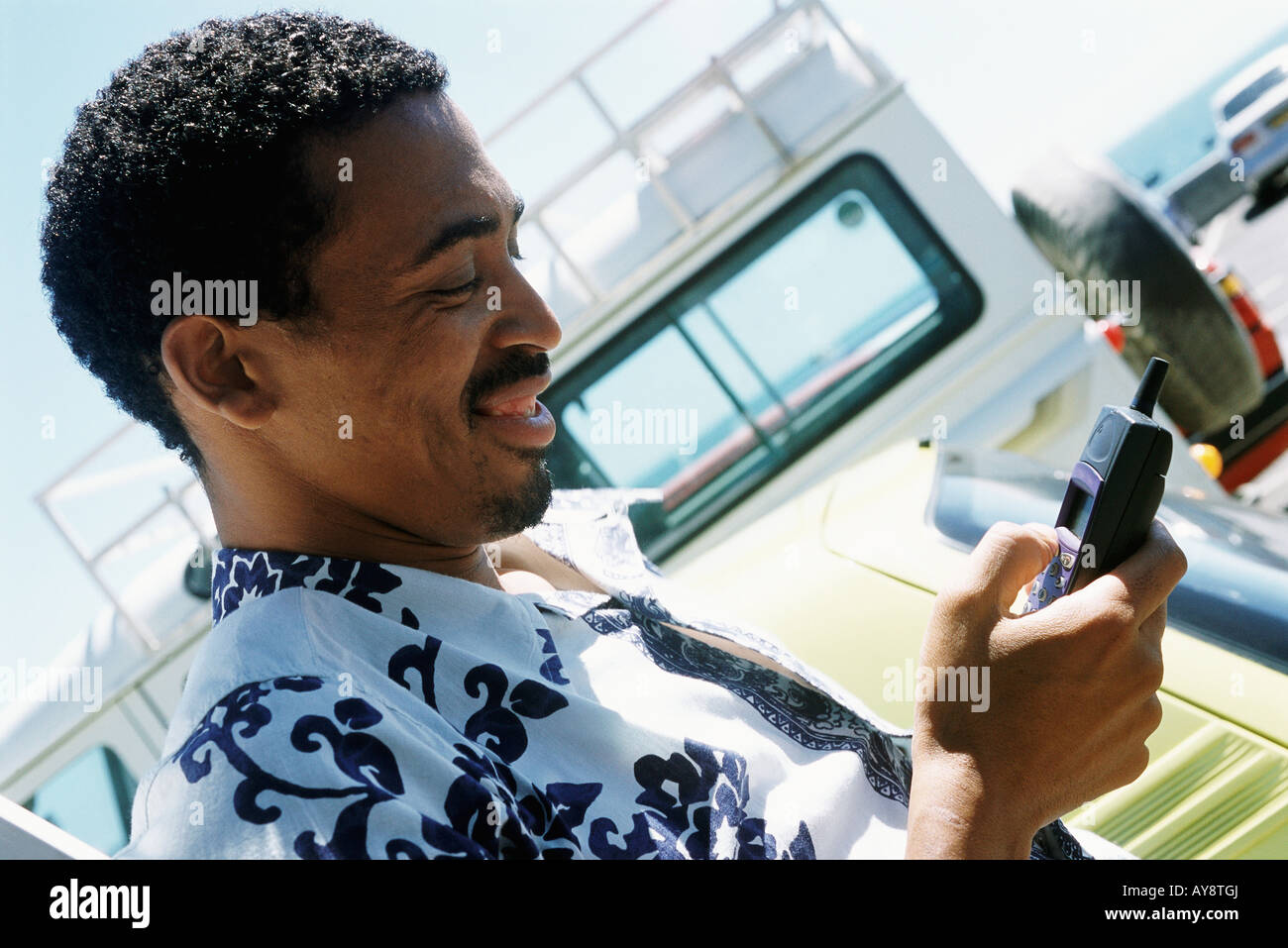 Mann im Hawaiihemd im Freien, blickte auf Handy, Lächeln Stockfoto