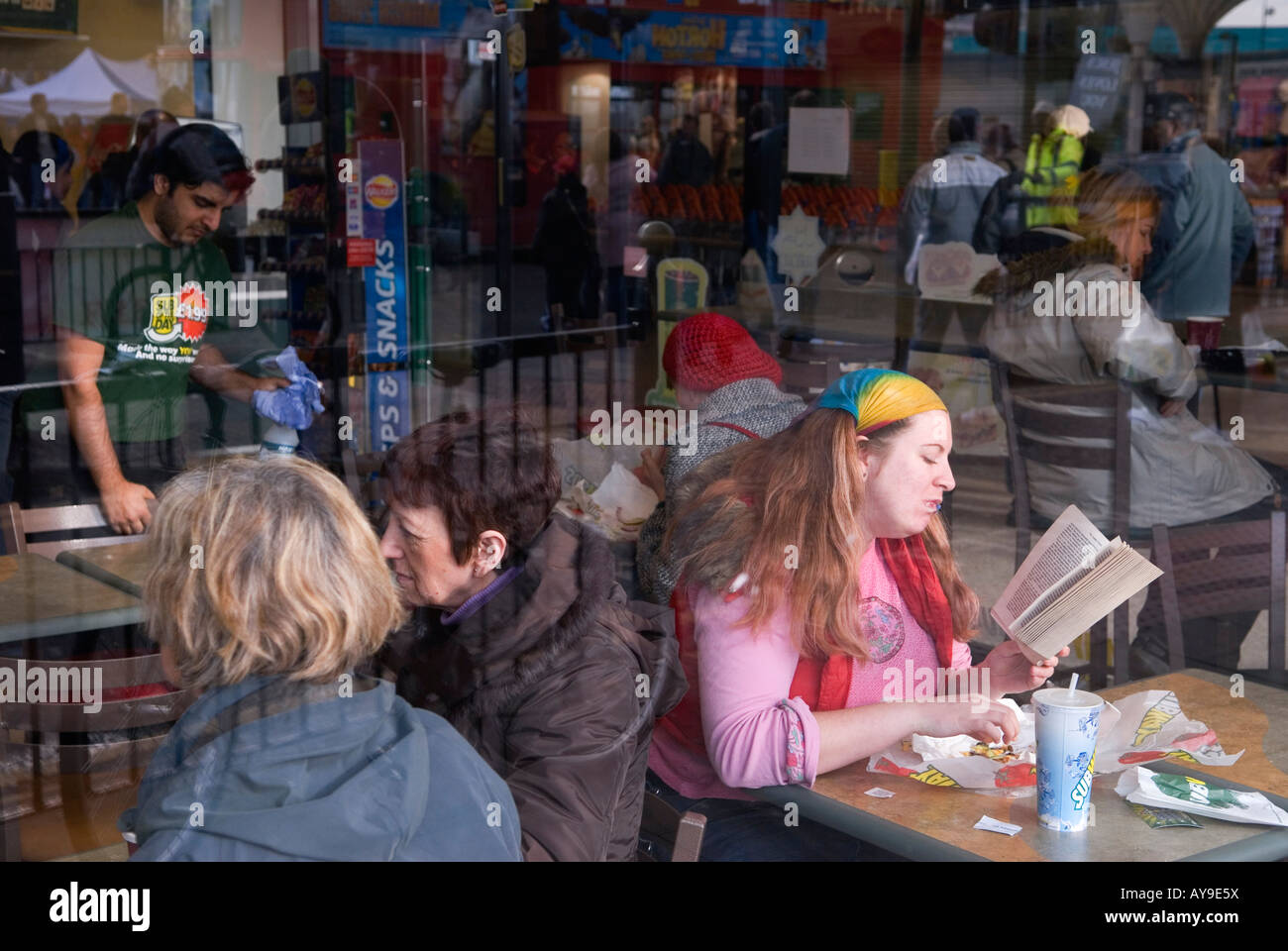 Frau in rosa mit regenbogenfarbenem Schal, der ihr Haar an Ort und Stelle hält. Lesebuch im Fast-Food-Outlet London 2008 2000s UK HOMER SYKES Stockfoto