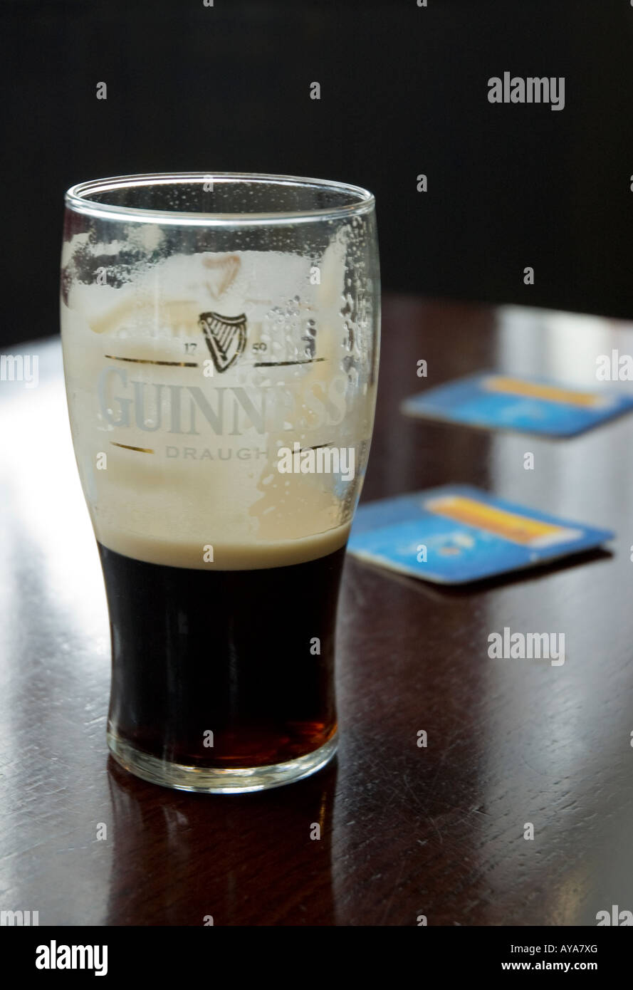 Guinness Pint Glas halb, am Nachbartisch Bierdeckel voll Stockfoto