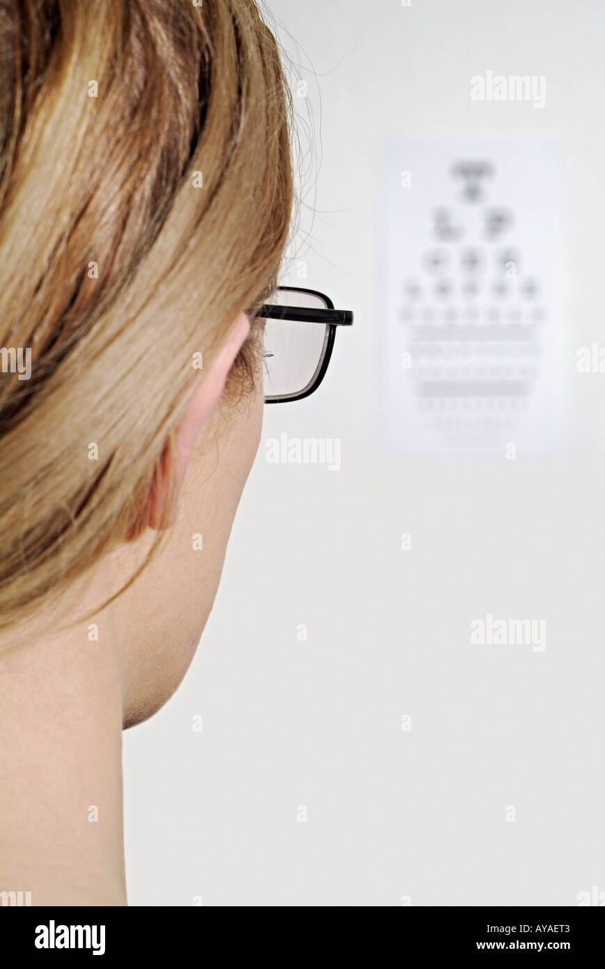 Frau, die ihre Sehkraft mit Brille geprüft durch das Lesen einer Snellen Diagramm auf einer Optiker-Wand Stockfoto