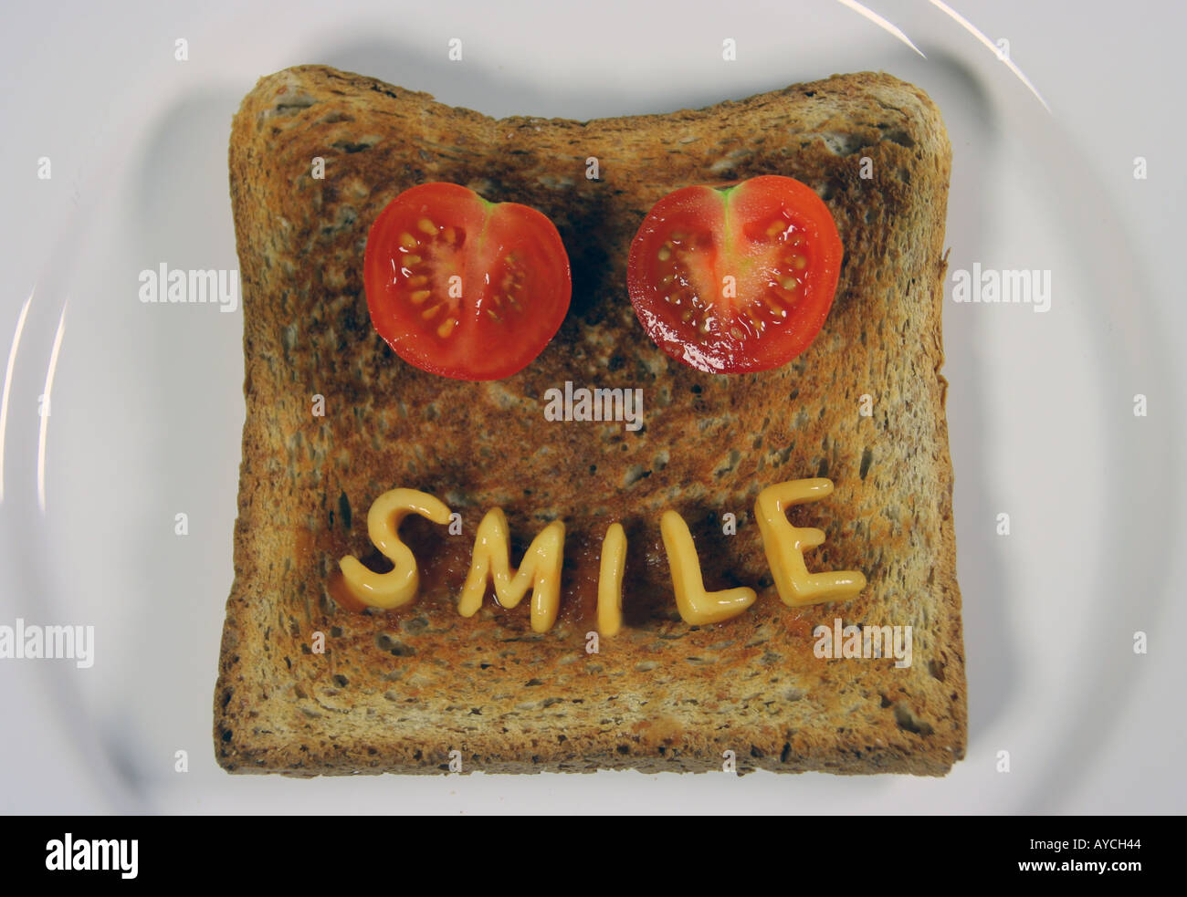 das Wort Lächeln auf Toast mit Alphabetti Spaghetti Nudelformen und zwei in Scheiben geschnittene Tomaten als Augen geschrieben Stockfoto