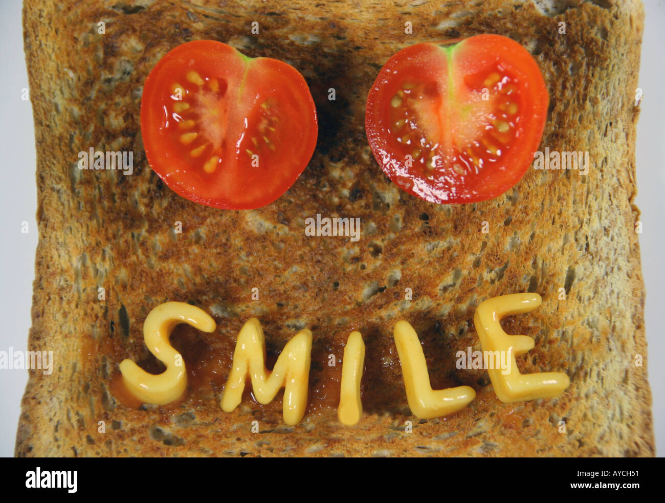 das Wort Lächeln auf Toast mit Alphabetti Spaghetti Nudelformen und zwei in Scheiben geschnittene Tomaten als Augen geschrieben Stockfoto