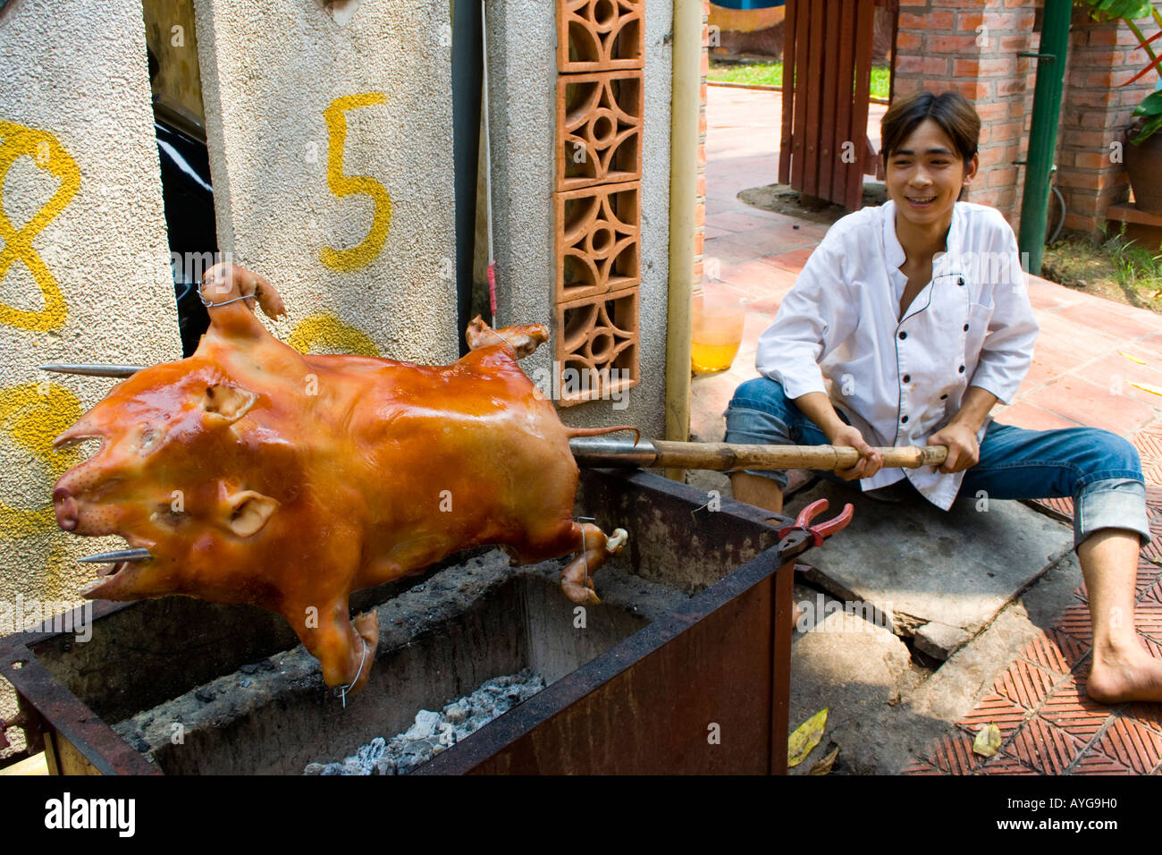 Junger Mann rösten ein Schwein über ein offener Grill-Hanoi-Vietnam Stockfoto