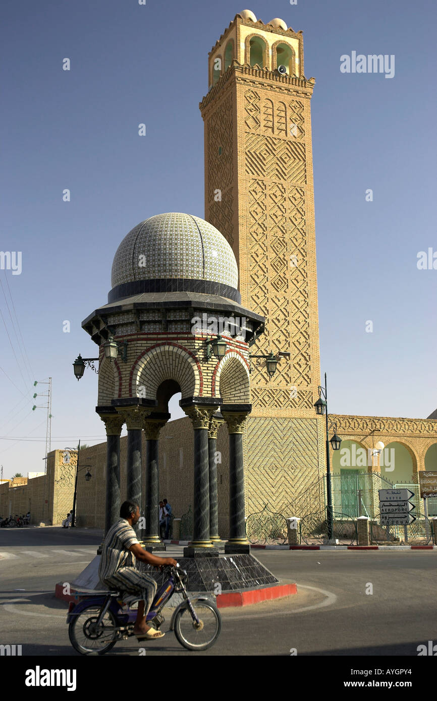 Motorradfahrer übergibt Moschee Minarett mit gemusterten Mauerwerk und stilisierte Kreisverkehr Tozeur Tunesien Stockfoto