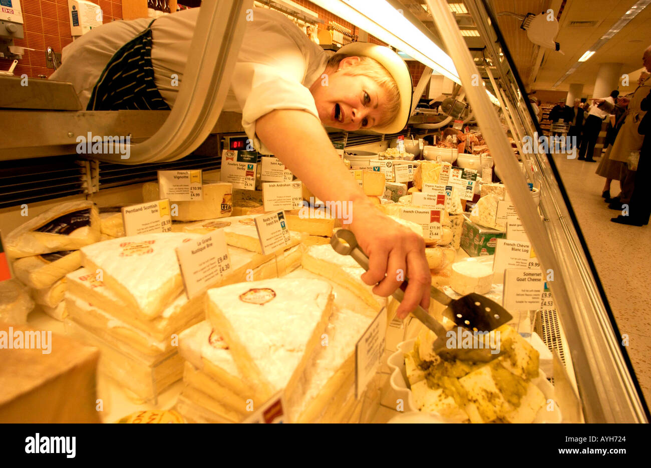 Ein Deli Helfer in Uniform und Hut erstreckt sich im Käse auf ihrer Käsetheke Waitrose-Supermarkt erreichen Stockfoto