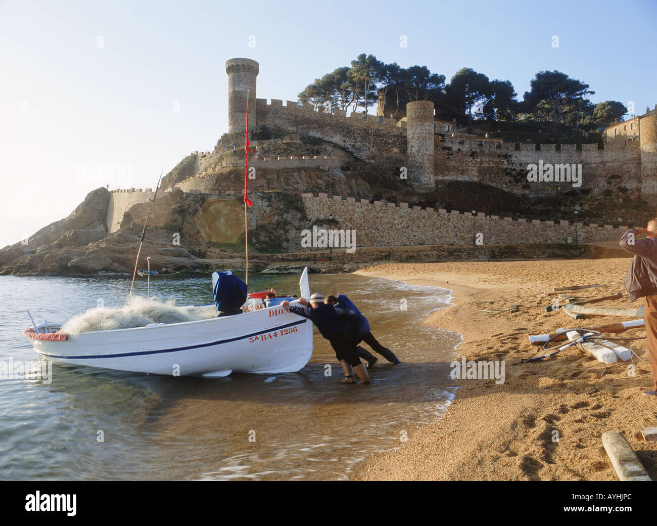 Fischer und Boot am Strand von Tossa De Mar in der Provinz Girona in Spanien bei Sonnenaufgang Stockfoto