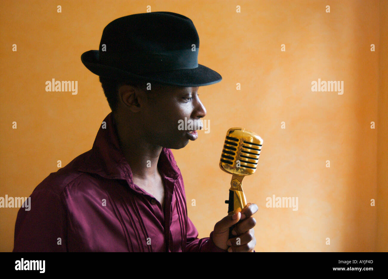 afroamerikanischer Mann mit schwarzem Hut ist sanft in einem altmodischen Goldenen Mikrofon singen. Stockfoto