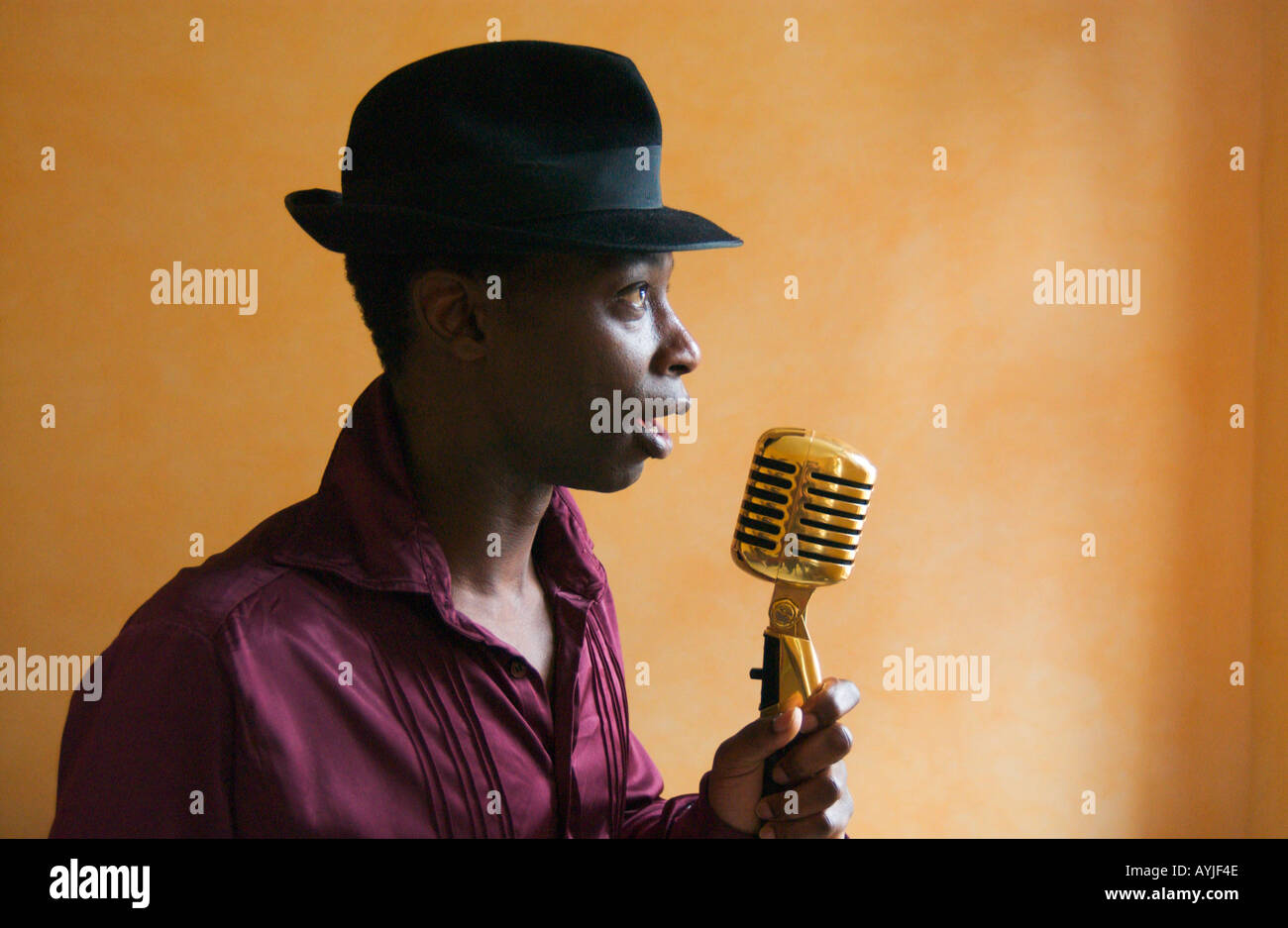 afroamerikanischer Mann mit schwarzem Hut ist sanft in einem altmodischen Goldenen Mikrofon singen. Stockfoto