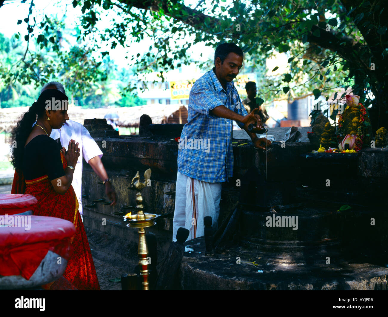 Kerala Indien-Shiva-Tempel Priester gießt heiliges Öl mit Frau beten und Götter mit Kurkuma Stockfoto