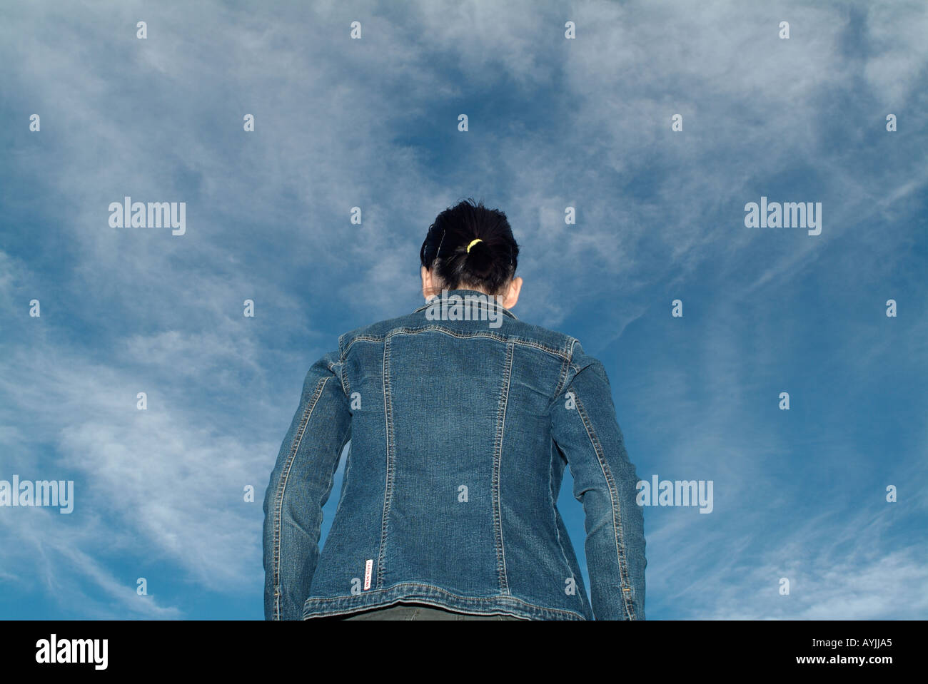 Woman Looking Out über einem blauen Wolkenhimmel, Rückansicht, flachen Winkel. Stockfoto