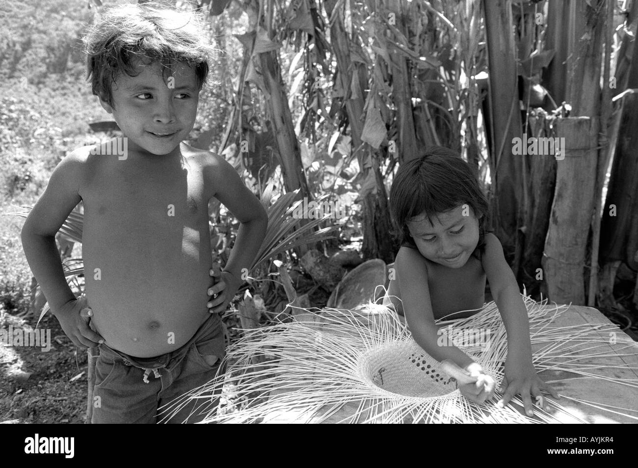 Schwarzweiß von zwei Kindern aus einer armen Bauernfamilie. Das sehr junge Mädchen macht Strohhüte, um das Einkommen der Familie zu ergänzen. Honduras Stockfoto