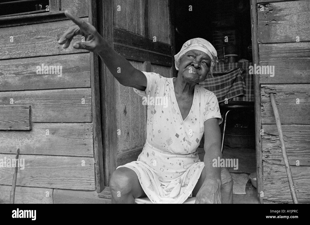 Ältere Frau, die vor ihrer Haustür in einem sehr armen Teil von Spanish Town, Jamaika sitzt Stockfoto