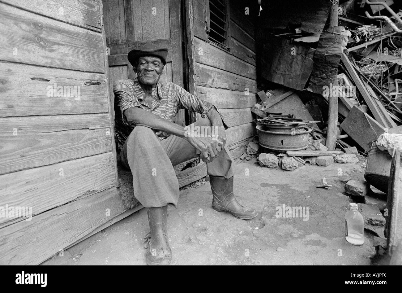 B/W eines älteren Mannes, der vor seiner Haustür sitzt und in extremer Armut im ärmsten Teil der spanischen Stadt lebt. Jamaika Stockfoto