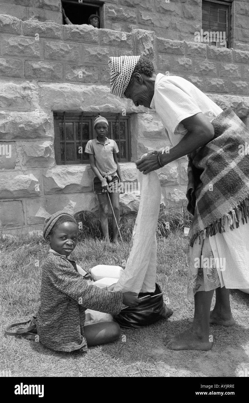 B/W eines Jungen und seiner Großmutter, die während einer längeren Dürreperiode Lebensmittelhilfe für Maismehl erhalten. Lesotho, Südliches Afrika Stockfoto