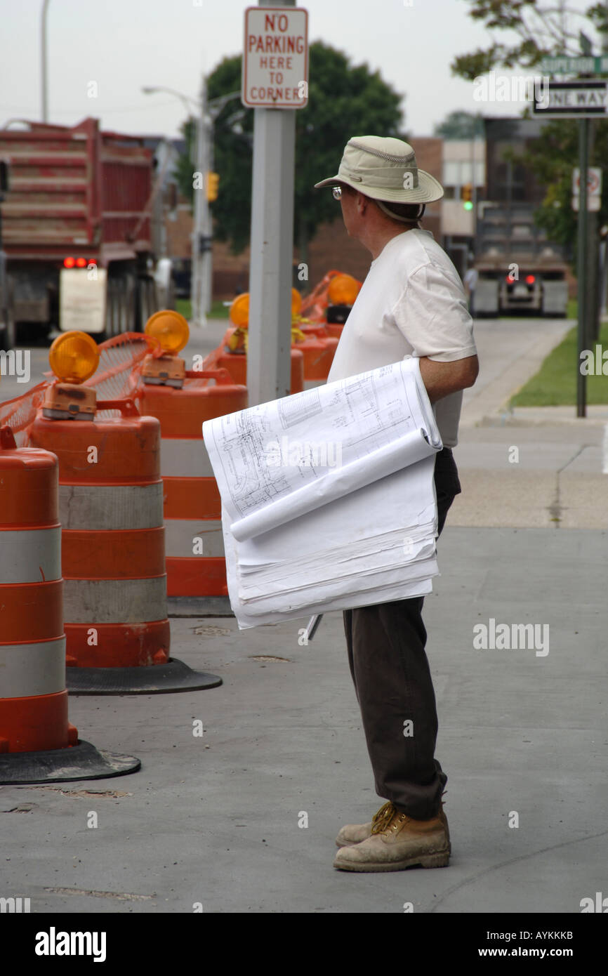 Erwachsene männliche Bauaufsichtsbeamte trägt seine Pläne und prüft auf den Fortgang der Arbeiten Stockfoto