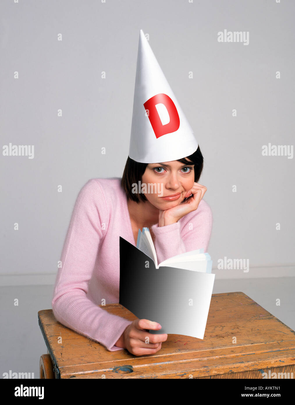 ziemlich ausgereift Student sucht glum in einem Klassenzimmer eine Dummköpfe Kappe trägt, während ein Buch zu lesen Stockfoto