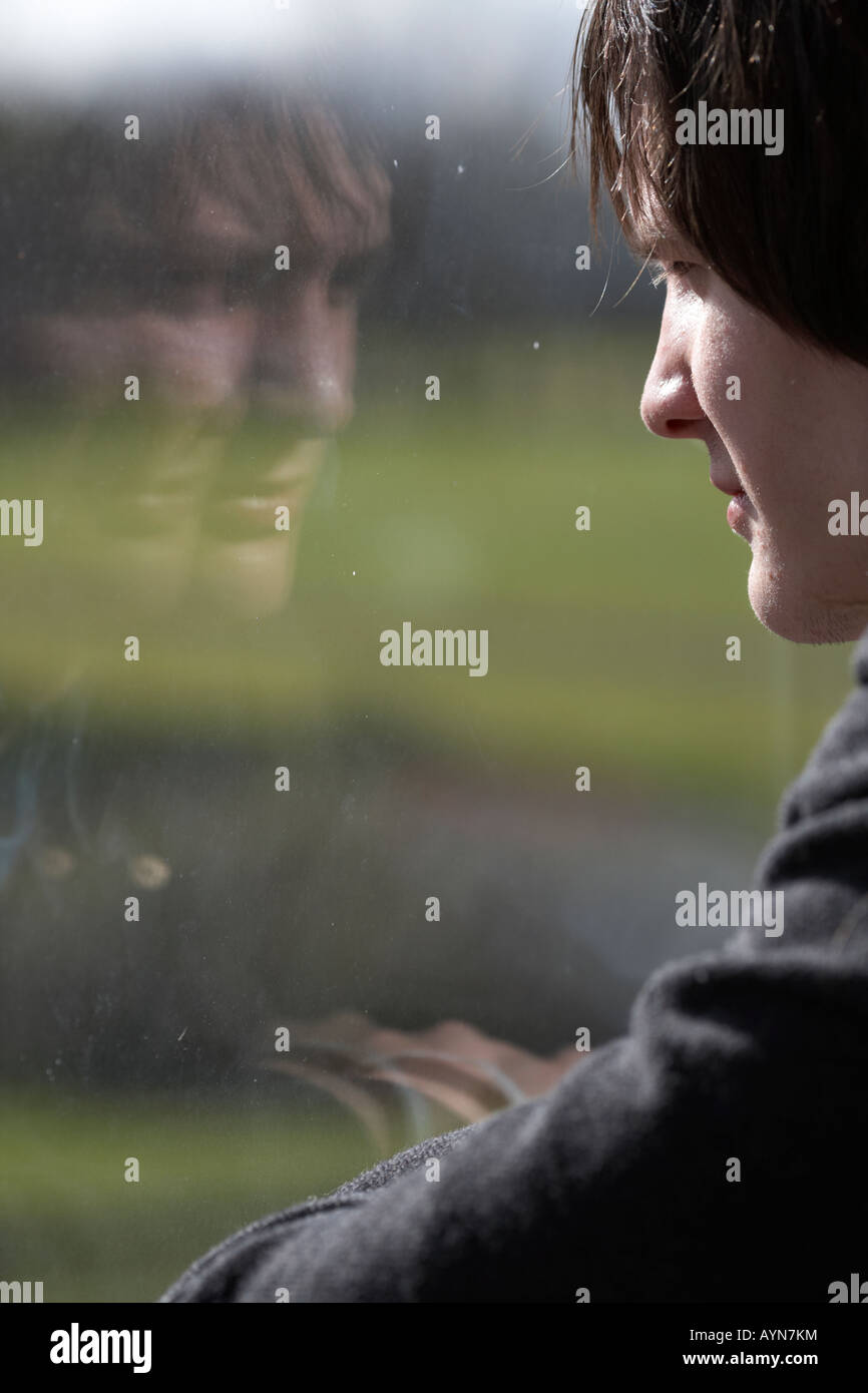 jungen dunkelhaarigen Teenager Mann starrt durch ein schmutziges Fenster mit Reflexion Stockfoto