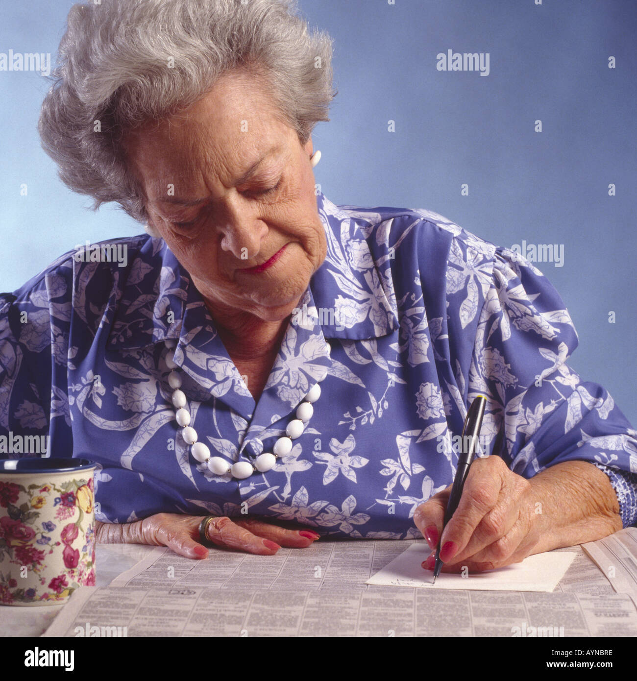 ältere Frau mit Zeitung klassifiziert Abschnitt Tisch Notizen Stockfoto