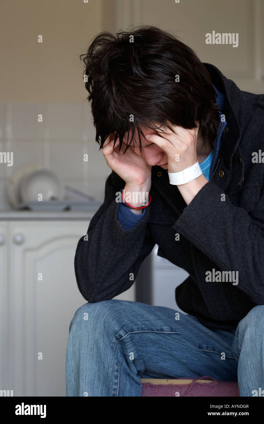 jungen dunkelhaarigen Teenager Mann sitzt mit seinem Kopf in seine Hände starrte auf den Boden Stockfoto
