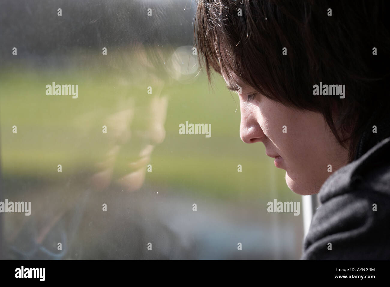 jungen dunkelhaarigen Teenager Mann starrt durch ein schmutziges Fenster mit Reflexion Stockfoto