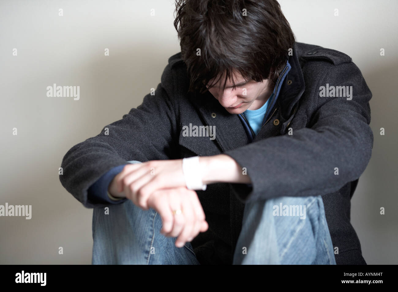 jungen dunkelhaarigen Teenager Mann sitzen auf dem Boden mit dem Rücken gegen die Wand in der fötalen Position nach unten Stockfoto