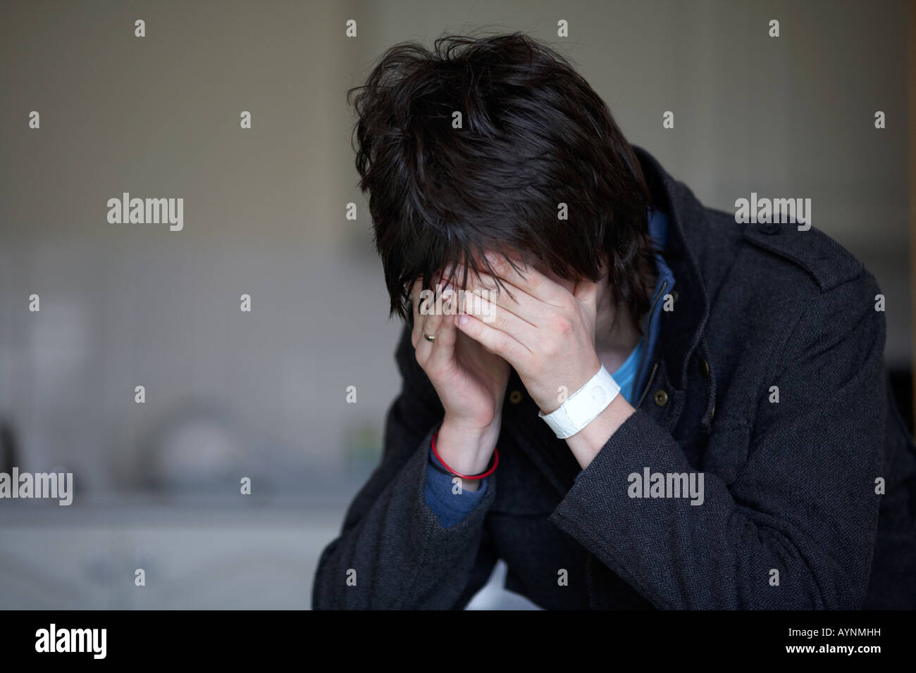 jungen dunkelhaarigen Teenager Mann sitzt mit seinem Kopf in seine Hände versteckt sein Gesicht starrte auf den Boden in der Küche Stockfoto
