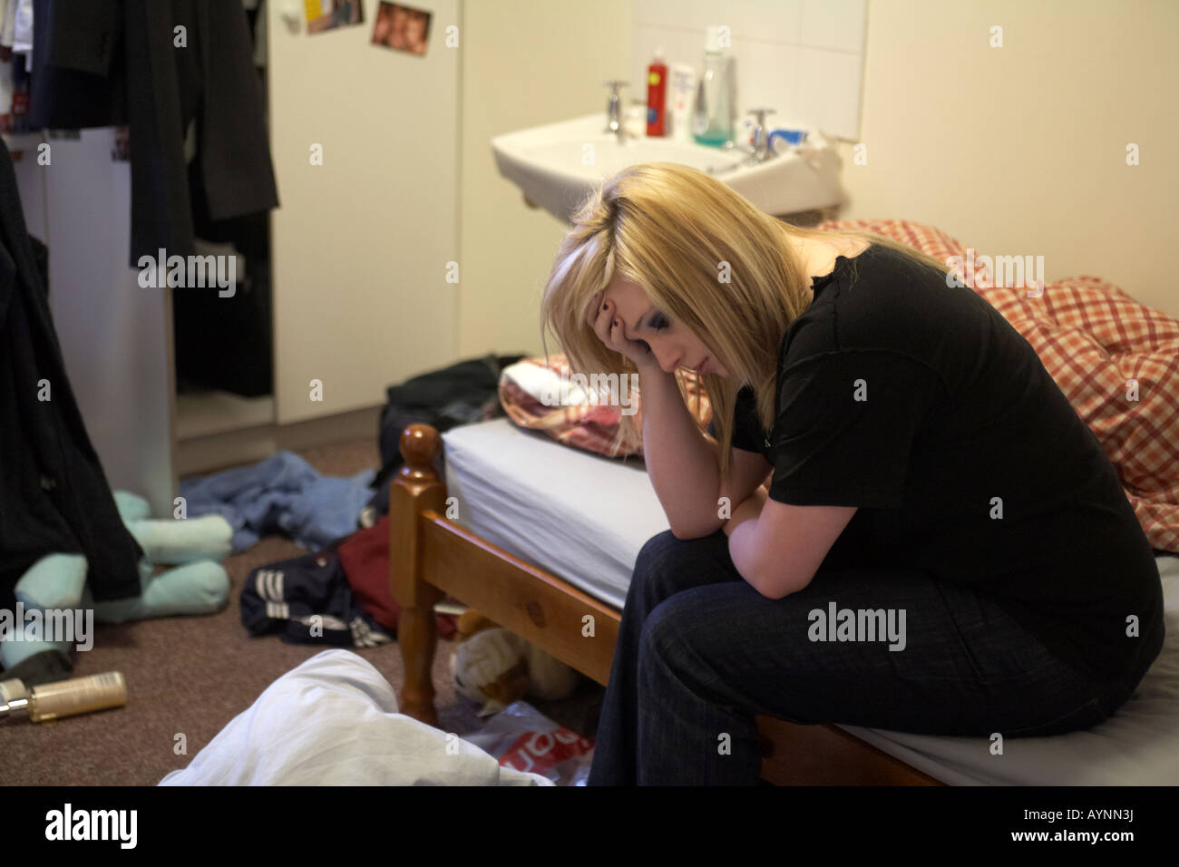 Junge Teenager Frau sitzt auf dem Bett in unordentlichen Hmo-Zimmer-appartment Schlafzimmer ihren Kopf mit einer Hand Stockfoto