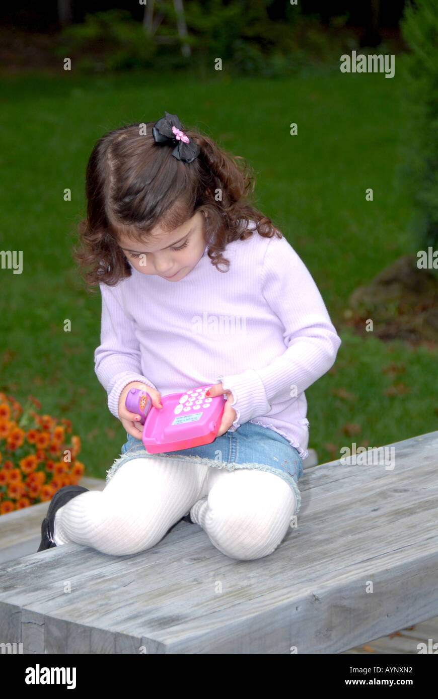 Drei Jahre altes Mädchen zusammengerollt auf Außenbank blickte auf ein Spielzeug-Telefon Stockfoto