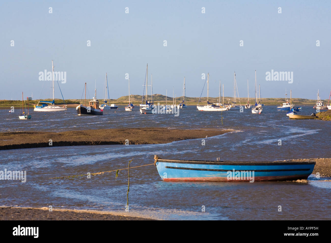 Boote vertäut am Brancaster Staithe North Norfolk England mit blauem Meer und klaren Sommerhimmel Stockfoto