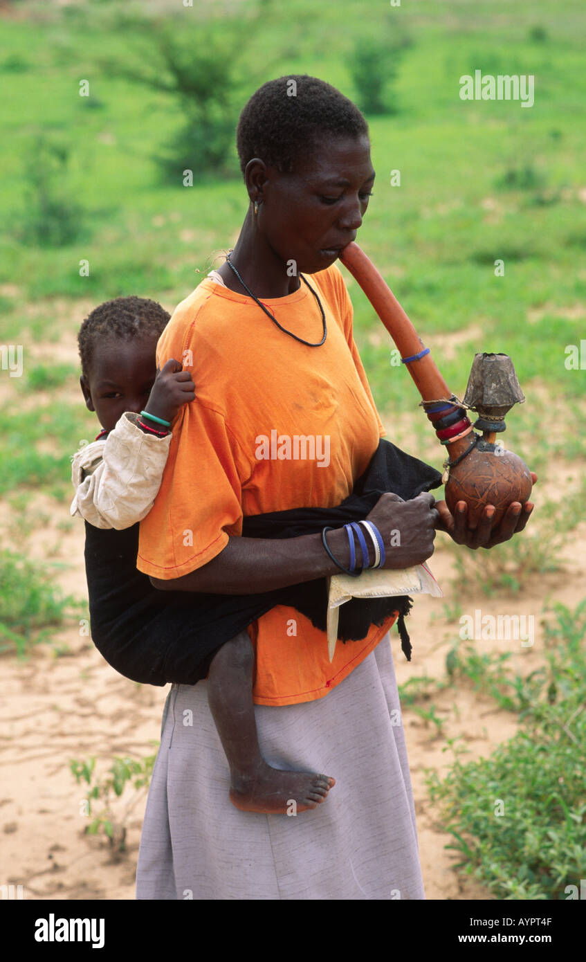 Batonga-Frau raucht traditionelle Wasserleitung und trägt ihr Kind auf dem Rücken. Nr Binga, Simbabwe Stockfoto