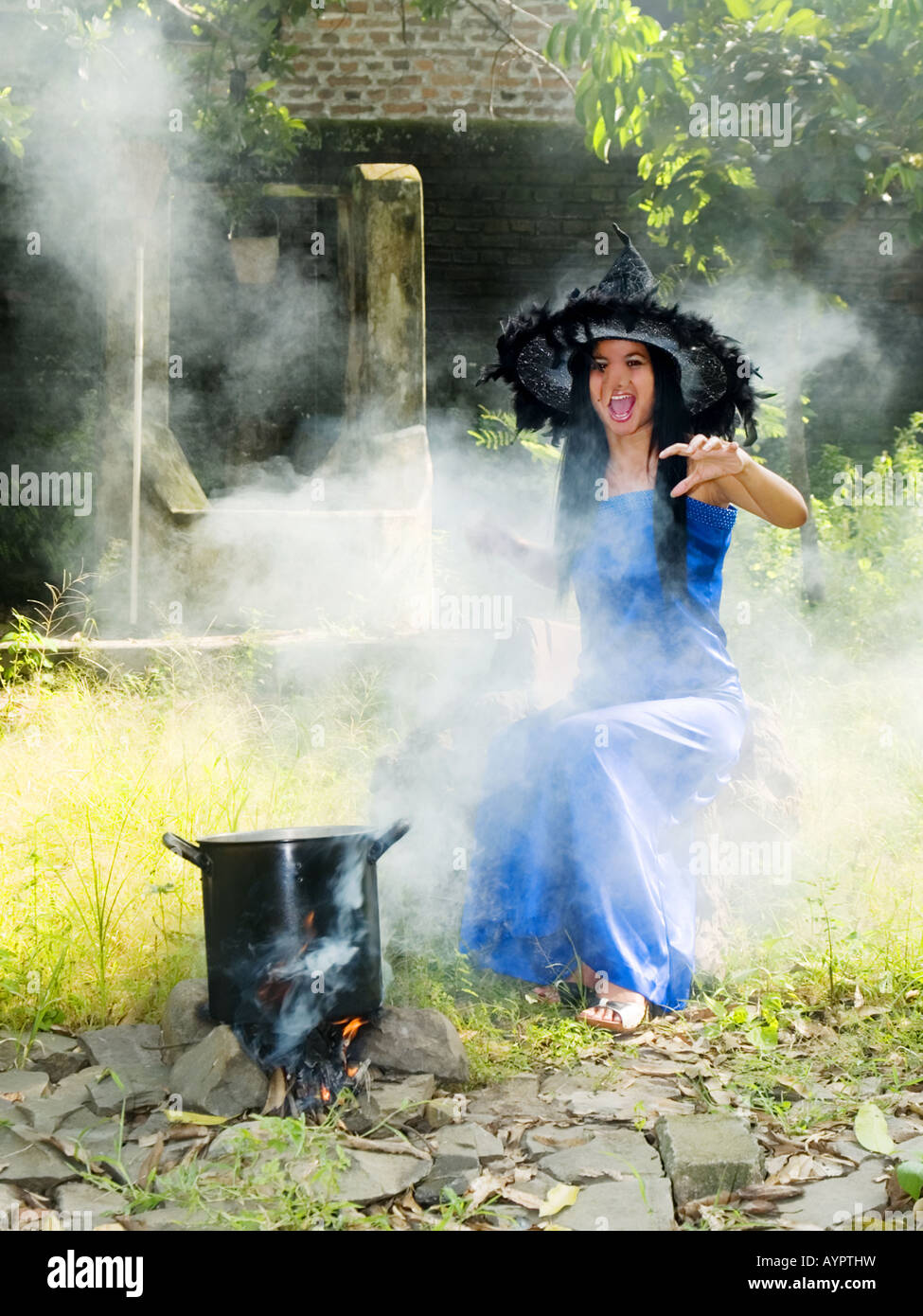 Junge, hübsche Hexe im blauen Kleid und Zipfelmütze wirft Zaubersprüche in einem Garten, Madiun, Ost-Java, Indonesien. Stockfoto