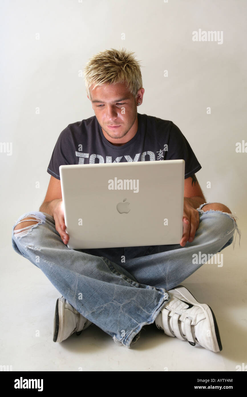 Zwanzig Jahre alten männlichen sitzen gekreuzten Beinen mit einem Apple Mac Laptop. Stockfoto
