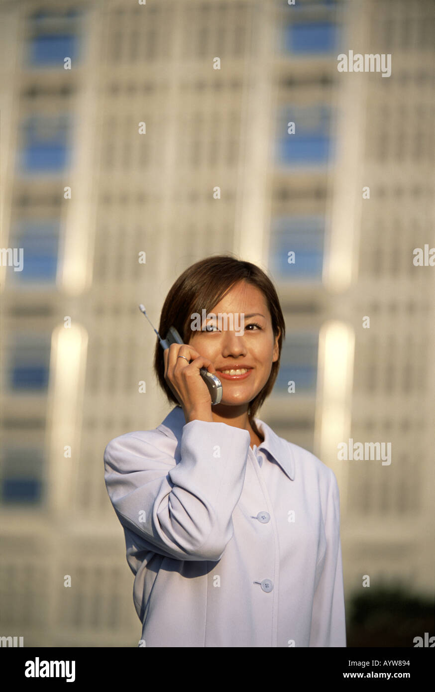 Frau im Gespräch über ein Handy mit hohen Bürogebäude im Hintergrund Stockfoto