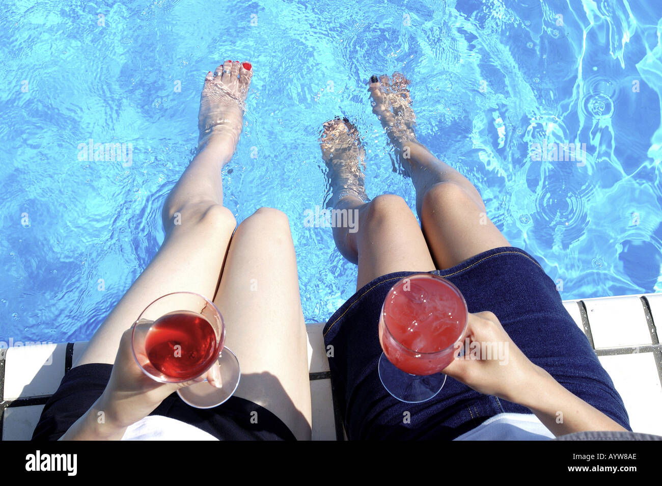 Zwei Frauen sitzen auf der Poolseite mit kalten Getränken Stockfoto