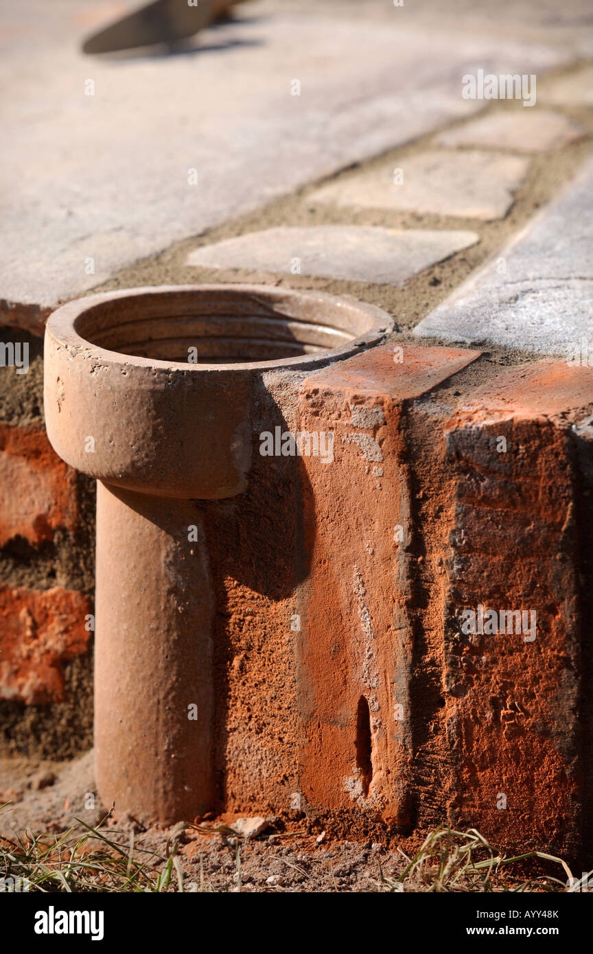 EINE IMPROVISIERTE BLUMENTOPF HERGESTELLT VON EINEM TEIL DER ALTEN LEHM FALLROHR EINGEBAUT IN EINEN INNENHOF MIT NATURSTEINPLATTEN UK GELEGT Stockfoto