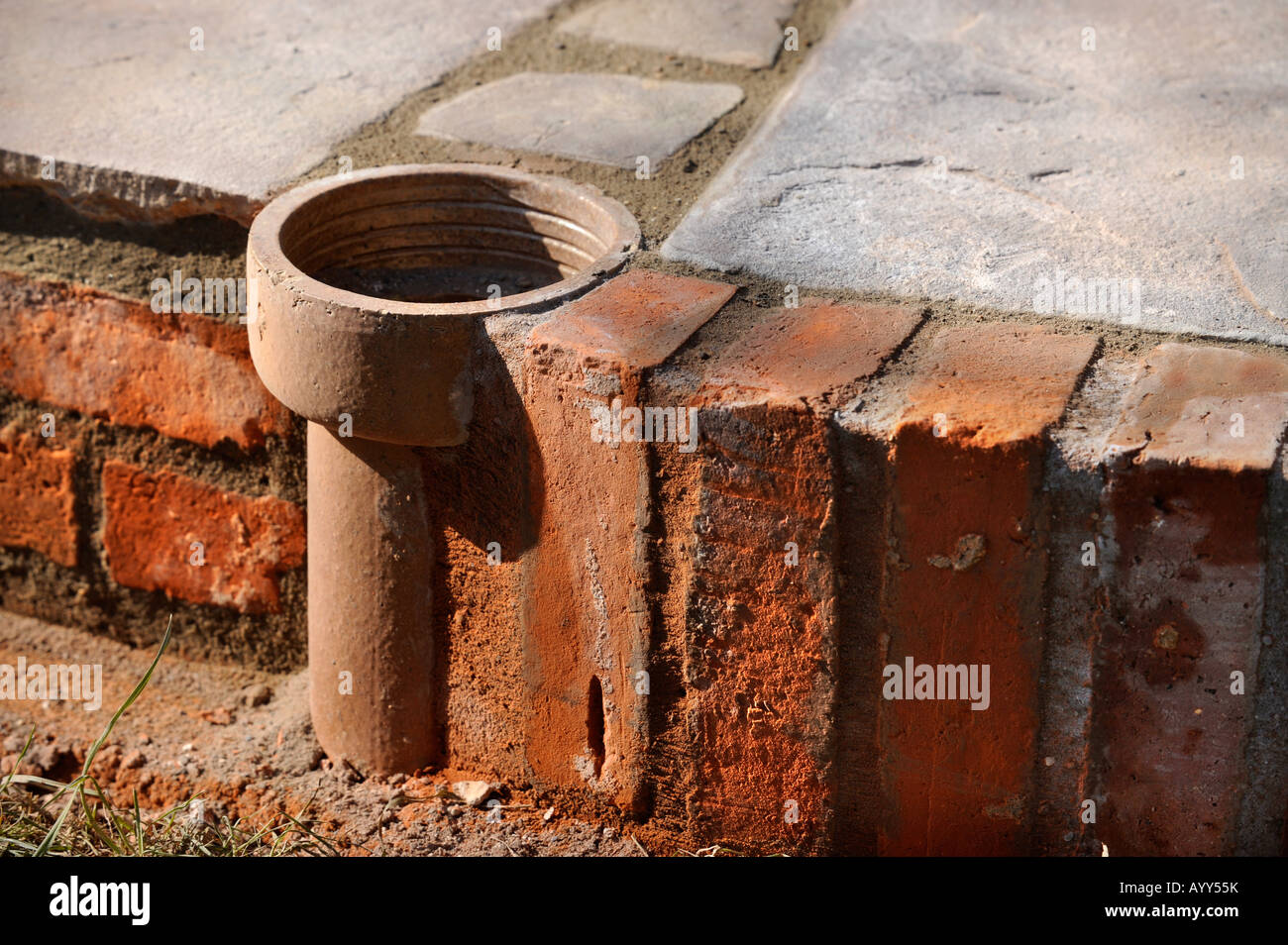 EINE IMPROVISIERTE BLUMENTOPF HERGESTELLT VON EINEM TEIL DER ALTEN LEHM FALLROHR EINGEBAUT IN EINEN INNENHOF MIT NATURSTEINPLATTEN UK GELEGT Stockfoto